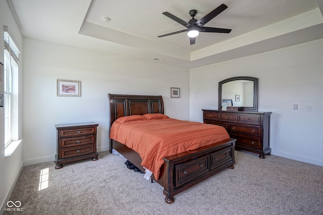 carpeted bedroom with baseboards, a tray ceiling, and ceiling fan