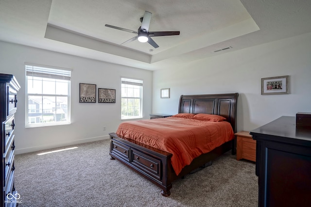 carpeted bedroom with a raised ceiling, multiple windows, baseboards, and ceiling fan