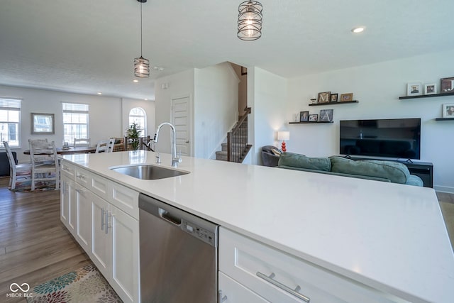 kitchen featuring stainless steel dishwasher, a sink, white cabinetry, light countertops, and decorative light fixtures