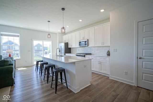 kitchen featuring stainless steel appliances, wood finished floors, a center island with sink, decorative backsplash, and a kitchen bar