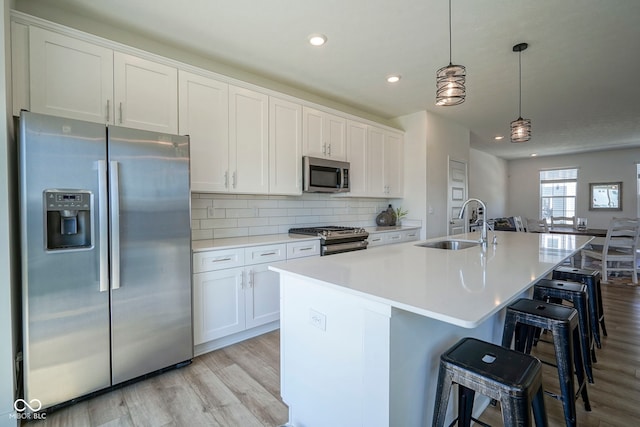 kitchen featuring stainless steel appliances, a sink, light wood-style flooring, white cabinets, and an island with sink