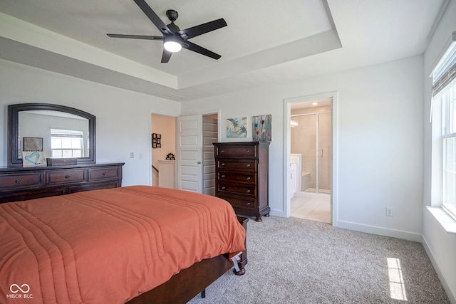 bedroom with a raised ceiling, light carpet, ensuite bath, and baseboards
