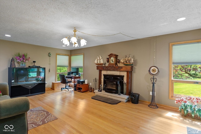 living room featuring a chandelier, wood finished floors, a textured ceiling, a glass covered fireplace, and an office area