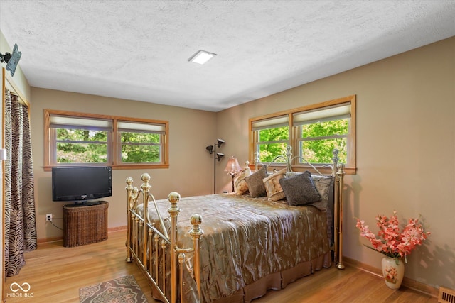 bedroom featuring wood finished floors, a textured ceiling, baseboards, and multiple windows