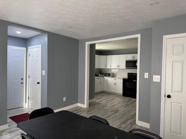 322 S Rural St, Indianapolis, IN 46201 - kitchen featuring black range with electric cooktop, stainless steel microwave, baseboards, white cabinets, and a textured ceiling