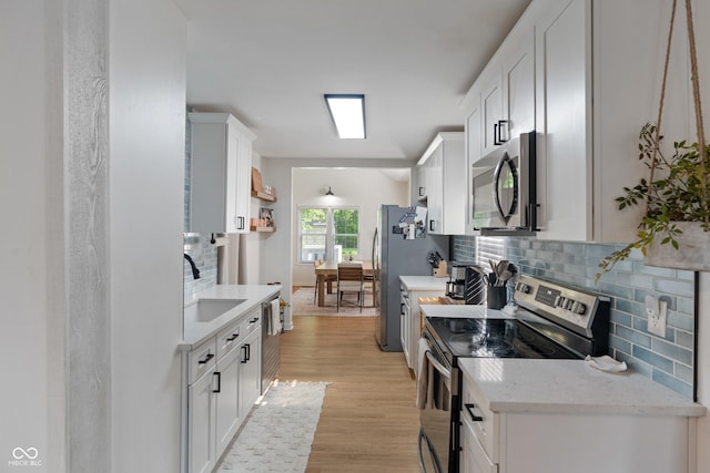 1802 E 66th St, Indianapolis, IN 46220 - kitchen featuring appliances with stainless steel finishes, a sink, backsplash, white cabinets, and light wood-style flooring