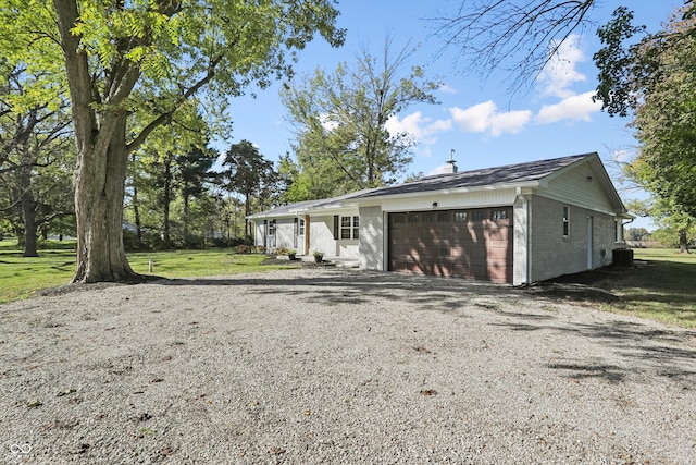 view of front of house featuring an attached garage, brick siding, gravel driveway, and a front lawn