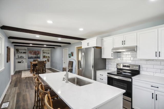 kitchen with appliances with stainless steel finishes, under cabinet range hood, dark wood finished floors, a sink, and beamed ceiling