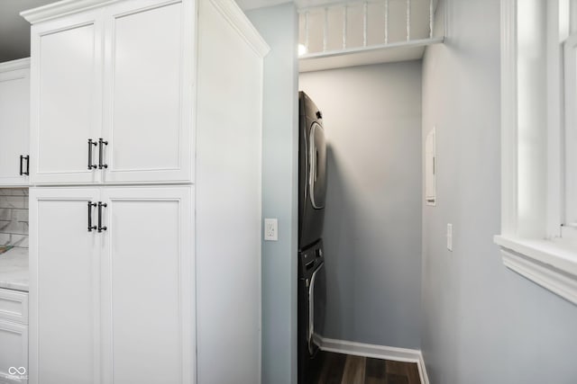 washroom with stacked washer / drying machine, baseboards, dark wood-type flooring, and cabinet space