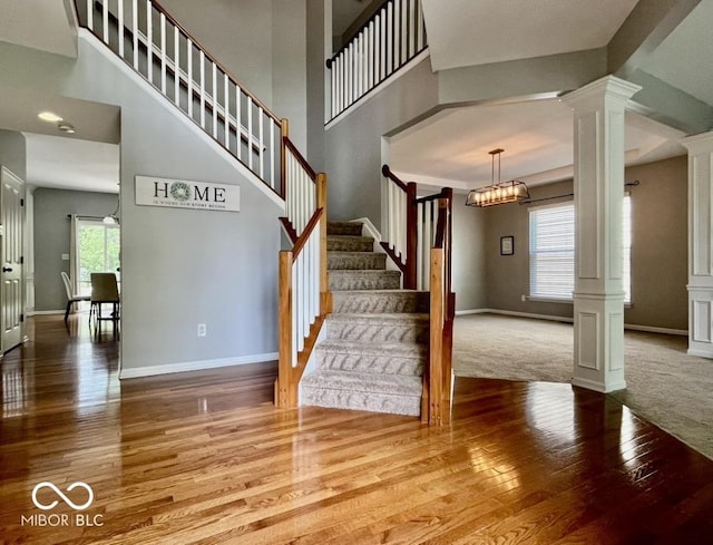 stairs with hardwood / wood-style flooring, decorative columns, baseboards, and a high ceiling