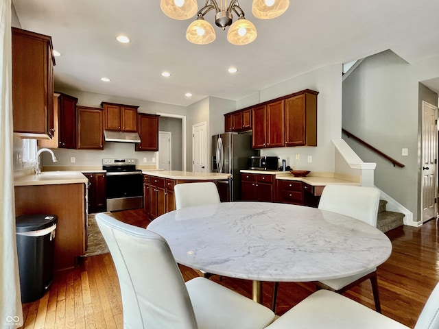 kitchen featuring stainless steel appliances, under cabinet range hood, a sink, wood-type flooring, and light countertops