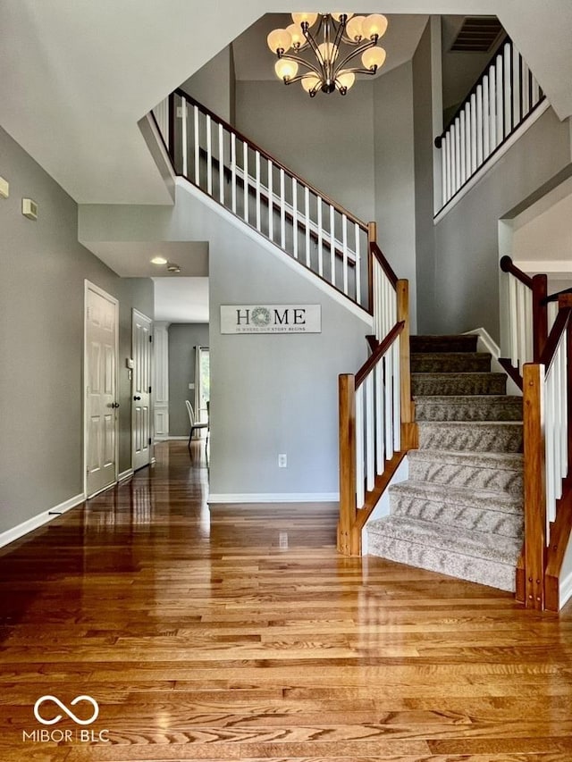 staircase featuring wood finished floors, a chandelier, a high ceiling, and baseboards