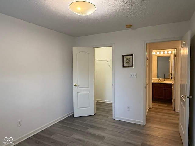 11523 Coastal Way, Indianapolis, IN 46229 - unfurnished bedroom featuring dark wood-style floors, baseboards, a walk in closet, a textured ceiling, and a sink