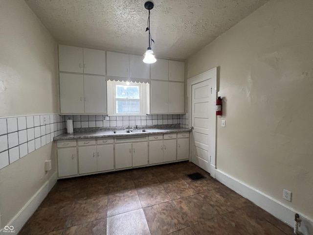 1137 W 34th St, Indianapolis, IN 46208 - kitchen featuring a textured ceiling, white cabinets, pendant lighting, a sink, and backsplash