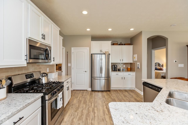 9166 Lieven St, Avon, IN 46123 - kitchen with stainless steel appliances, light wood-style floors, decorative backsplash, arched walkways, and white cabinetry