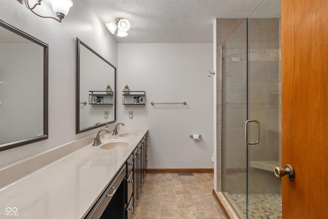 bathroom featuring a shower stall, a textured ceiling, double vanity, and baseboards
