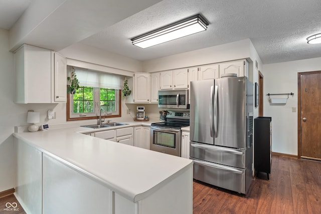 kitchen featuring appliances with stainless steel finishes, a sink, a peninsula, white cabinets, and a textured ceiling