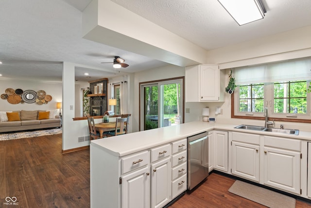 kitchen featuring stainless steel dishwasher, a sink, a peninsula, open floor plan, and white cabinets