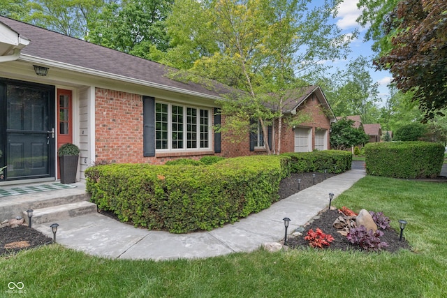 view of side of home featuring brick siding, a shingled roof, and a yard