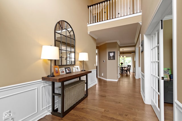 entryway with crown molding, wood finished floors, wainscoting, a decorative wall, and a high ceiling