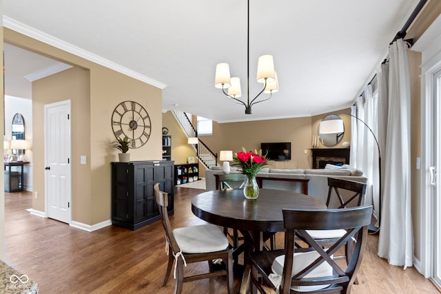 dining space featuring wood finished floors, crown molding, baseboards, a fireplace, and stairs