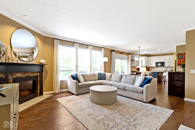 living area with crown molding, dark wood finished floors, recessed lighting, a stone fireplace, and baseboards