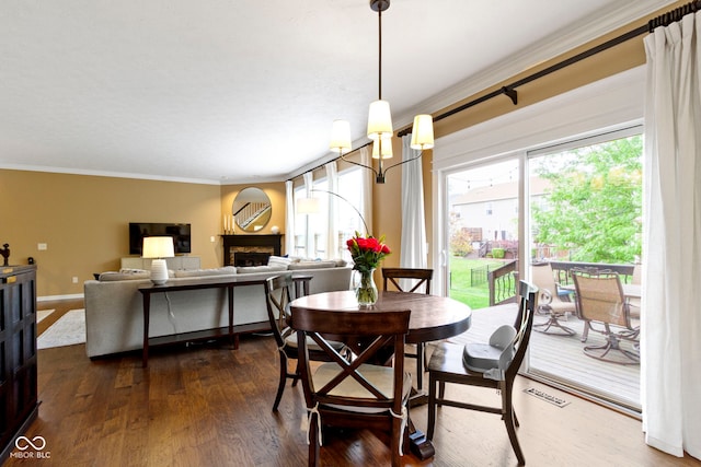 dining space featuring ornamental molding, healthy amount of natural light, dark wood-type flooring, and a fireplace