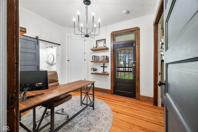office area featuring light wood finished floors, a barn door, baseboards, and a chandelier