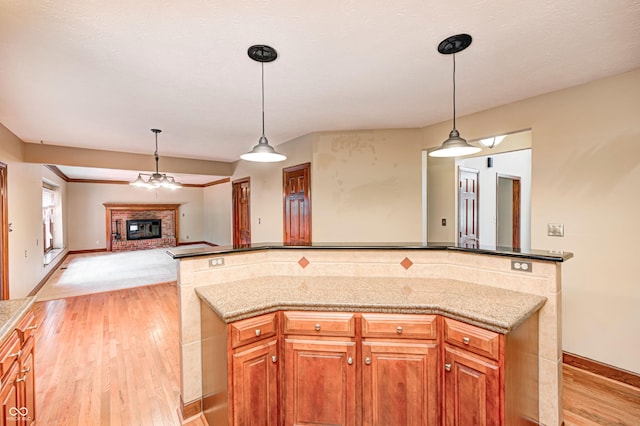 9158 Oak Knoll Ln, Fishers, IN 46037 - kitchen featuring light wood-style floors, a brick fireplace, a kitchen island, pendant lighting, and open floor plan