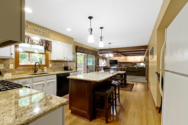 kitchen with black dishwasher, freestanding refrigerator, a sink, a kitchen island, and light wood-style floors