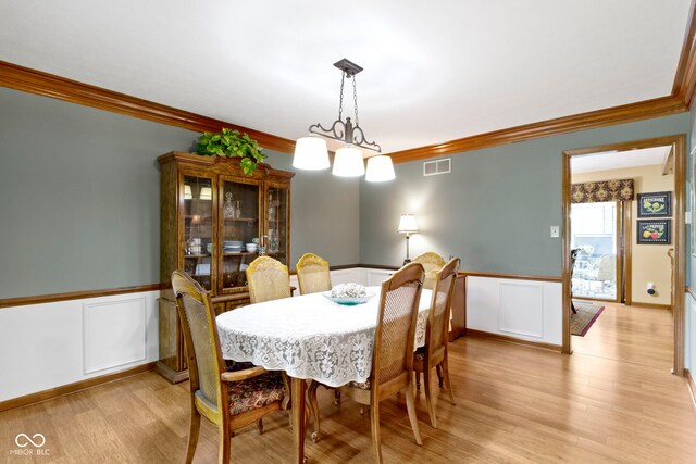 dining space featuring ornamental molding, wainscoting, light wood-style flooring, and a decorative wall