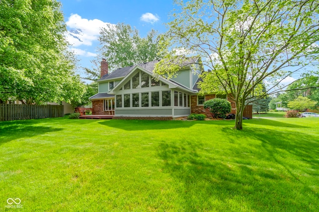 back of property with a sunroom, brick siding, a deck, and a chimney
