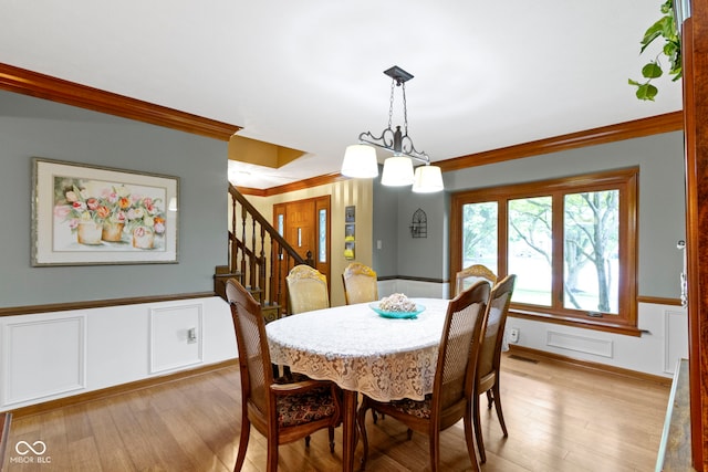 dining room with light wood-type flooring, a wainscoted wall, crown molding, a decorative wall, and stairway