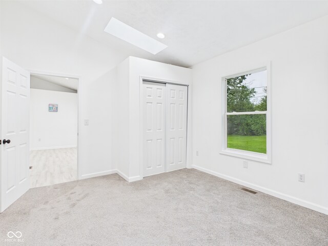 unfurnished bedroom with a skylight, carpet, baseboards, a closet, and vaulted ceiling