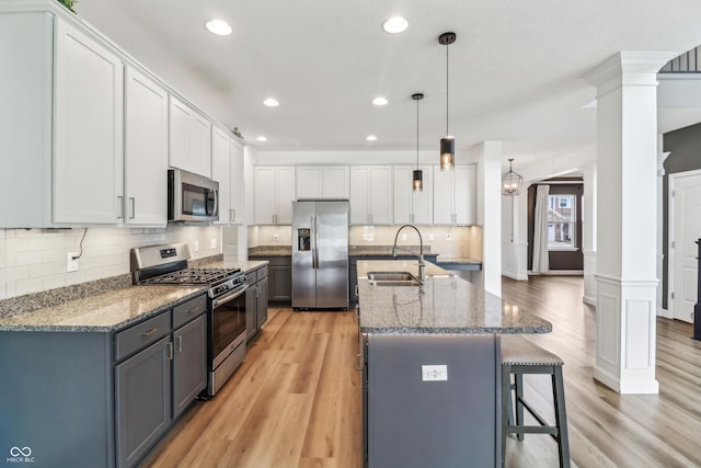 951 Parker Ln, Westfield, IN 46074 - kitchen featuring stainless steel appliances, decorative columns, a sink, light wood-style flooring, and an island with sink
