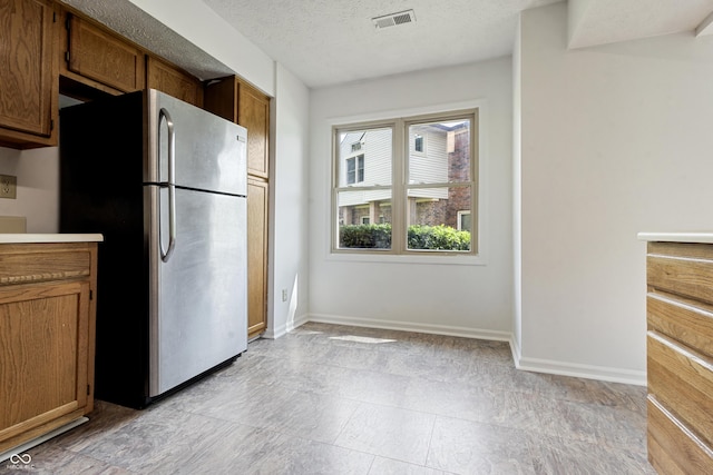 9572 Maple Way, Indianapolis, IN 46268 - kitchen featuring freestanding refrigerator, baseboards, brown cabinets, a textured ceiling, and light countertops