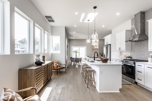 43 N Walcott St, Indianapolis, IN 46201 - kitchen with appliances with stainless steel finishes, wall chimney range hood, a kitchen bar, light wood-style floors, and backsplash