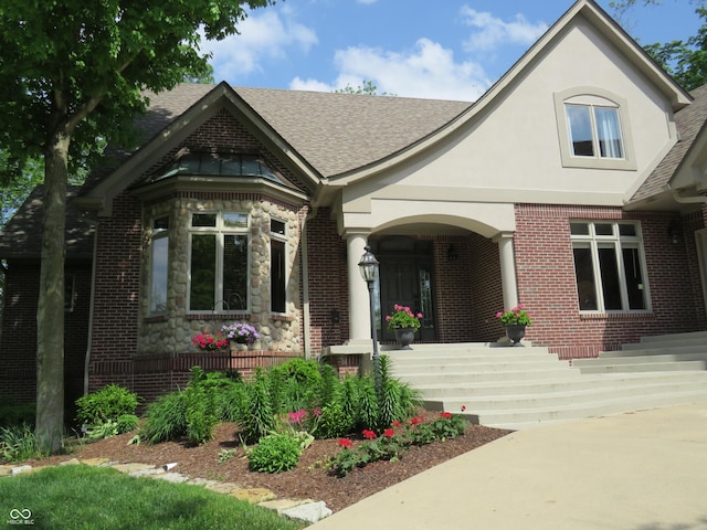 view of front facade with stucco siding, a porch, roof with shingles, brick siding, and stone siding