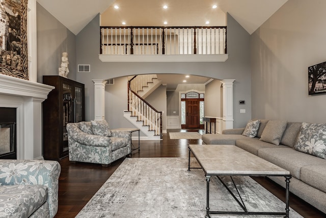 living area with dark wood-style flooring, ornate columns, arched walkways, a towering ceiling, and wainscoting
