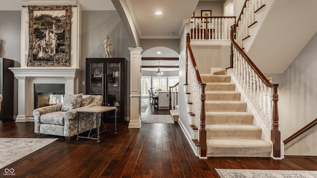 foyer entrance featuring arched walkways, hardwood / wood-style floors, crown molding, ornate columns, and stairs