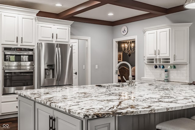 kitchen featuring stainless steel appliances, beam ceiling, light stone countertops, white cabinets, and a sink