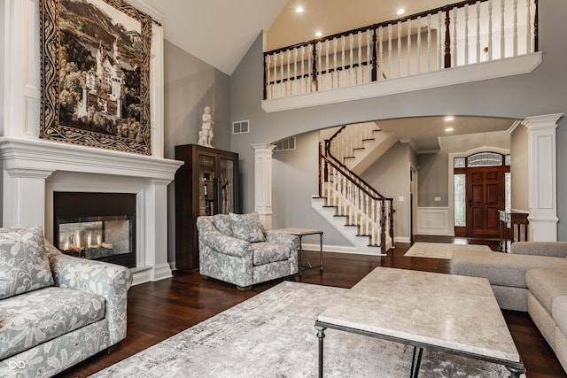 living area with ornate columns, high vaulted ceiling, dark wood-style flooring, stairs, and arched walkways