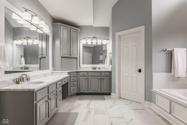 bathroom featuring marble finish flooring, two vanities, a garden tub, and baseboards