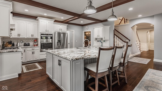 kitchen with stainless steel appliances, a sink, arched walkways, dark wood-style floors, and decorative backsplash