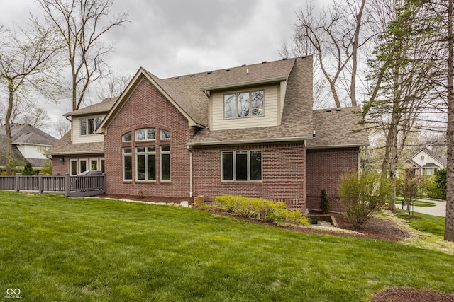 back of house with brick siding, roof with shingles, a yard, and a deck