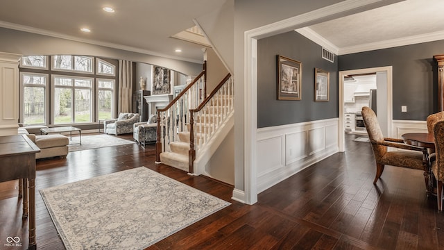 entrance foyer with dark wood-type flooring, crown molding, stairs, wainscoting, and a fireplace