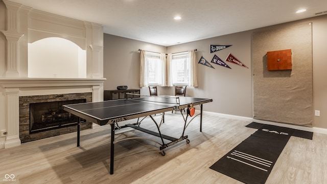 recreation room with light wood-type flooring, a stone fireplace, recessed lighting, and baseboards