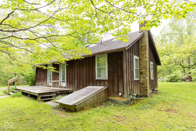 view of side of property with a chimney, a wooden deck, a yard, and a shingled roof