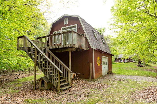 rear view of property with a gambrel roof, a deck, stairway, driveway, and a shingled roof