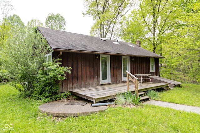 view of front of property featuring roof with shingles, a chimney, a front yard, and a deck